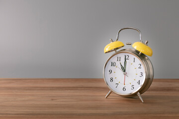 Retro silver alarm clock. 11:00.  am,  pm. Neutral background. Brown wood surface. Horizontal  photography with empty space for text or image.