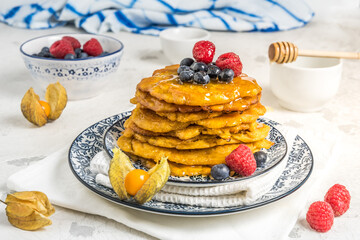 Pile of vegan pancakes with berries and syrup on a blue-white patterned plate on white background