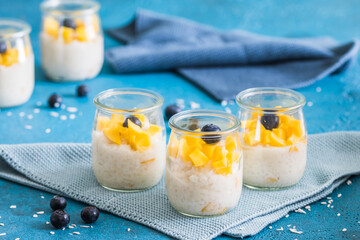 Coconut rice pudding with mango in dessert glasses on blue background