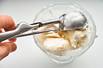A human hand puts a scoop of ice cream into a glass bowl with a scoop. Close-up