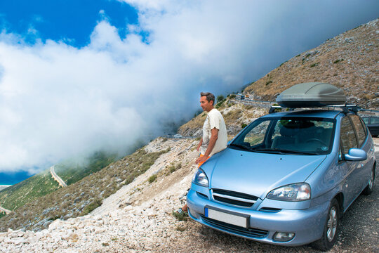 Tourist man with his car near Llogara Pass. White fog high in mountains. View from highlands on serpentine road. Albania.