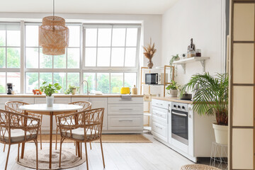 Interior of light kitchen with white counters, dining table and big window