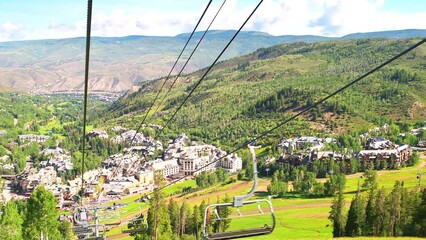 Beaver Creek ski resort with riding ski lift gondola in summer, Vail Resorts village buildings town with mountains point of view panning shot