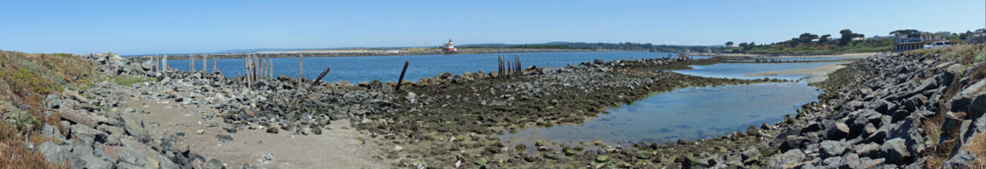 Panoramic of Coquille River where it enters the Pacific ocean.  Old pilings and barnacle covered rocks in foreground with the Coquille light house in the background