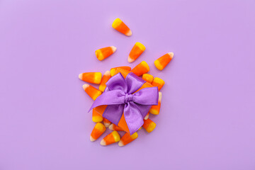 Gift box and tasty candy corns for Halloween on purple background