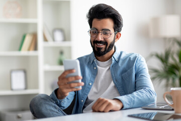 Great App. Smiling Indian Man Using Smartphone At Home Office