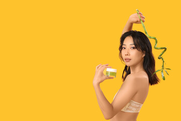 Beautiful young Asian woman with scrub and bamboo on yellow background