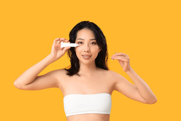 Beautiful young Asian woman with cream on yellow background