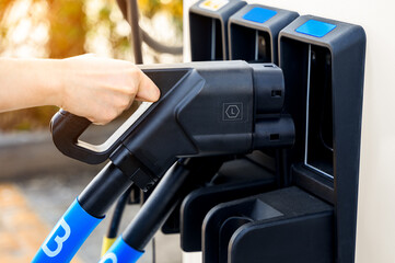 Hand holding probe charger in electric vehicle charging station with plug of power cable supply for Ev car, Green energy concept