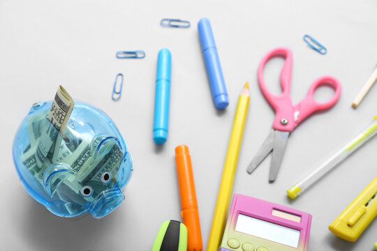 Piggy bank with money and different stationery on grey background