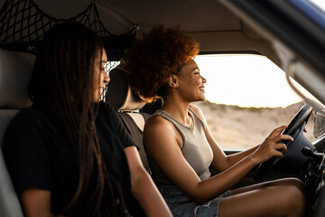 Two dark-skinned girls are driving a camper van to go on vacation. The woman with the afro hair...