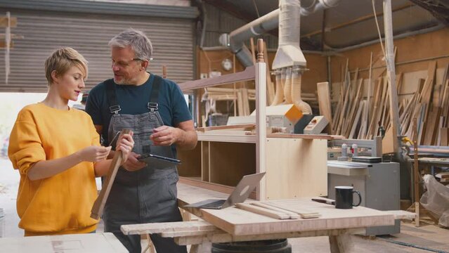 Mature male carpenter with digital tablet sharing woodworking skills with female apprentice in furniture factory - shot in slow motion