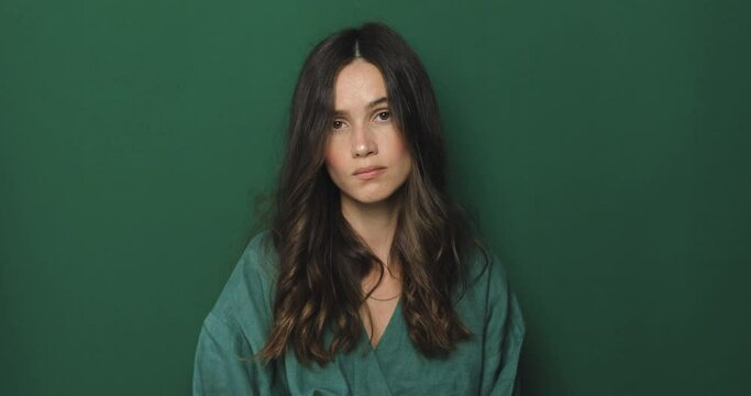 Brunette curly woman threatens with a fist is isolated on green background, shows fist has annoyed face expression going to revenge or threaten someone makes serious look. I will show you who is boss.