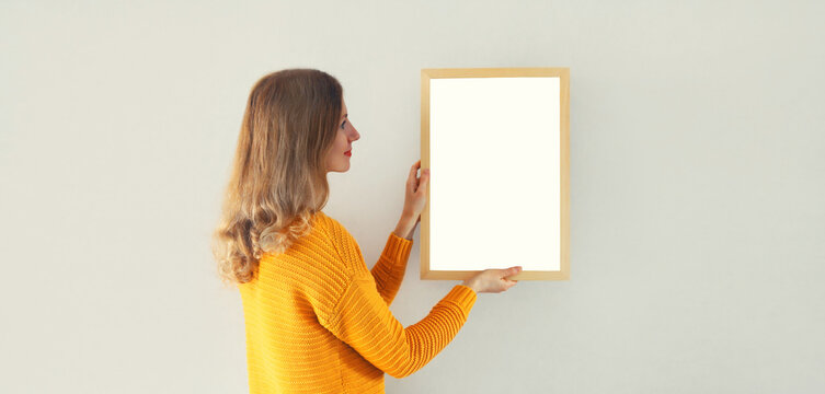 Young Woman Decorating Interior, Hanging Blank A Photo Frame Mockup On White Wall In A New House