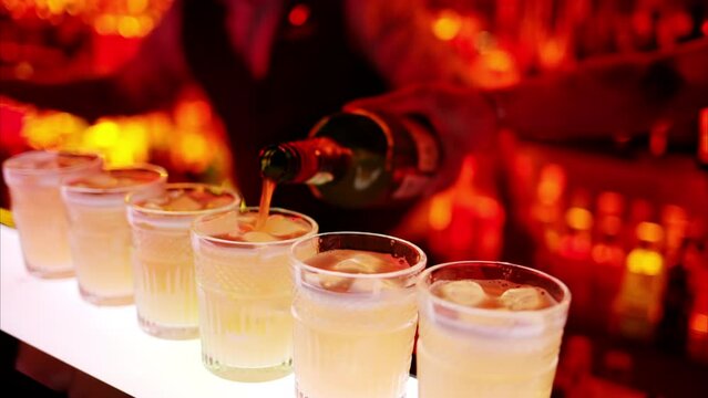 Barman making cocktails with whiskey liquor alcohol at the bar at night with red neon lights, slow motion