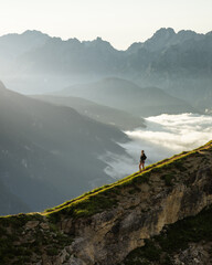 Woman walking along a ridge or fallout in the mountains, fog and beautiful mountain views of the Dolomites, Italy in the background.
