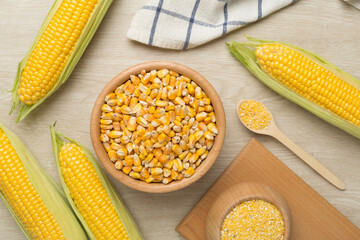 Corn groats and seeds with fresh cobs on wooden background, top view