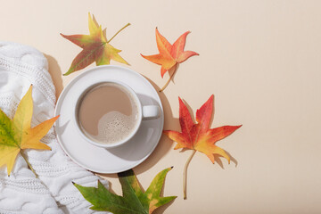 Obraz na płótnie Canvas Autumn flat lay. Cup of cocoa or coffee, women white sweater, autumn leaves on neutral background. Top view, copy space