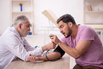 Fototapeta premium Old male doctor measuring young patient's blood pressure