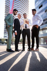 vertical team diverse male professionals look concentrated at team leader tablet. Colleagues serious expression gathered outside business building. Group confident office workers company together.