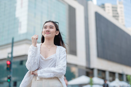 An optimistic young female office worker thinking and visualizing her success and promotion. Feeling bullish and cheerful. Outdoor city scene.