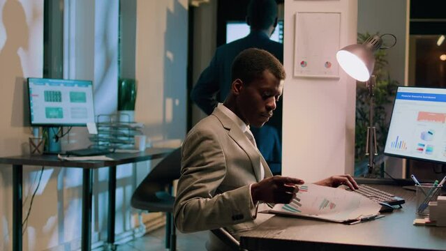 Bipoc coworkers auditing financial payroll reports and statistics on computer screen during nightshift. Adept businessmen working overnight on important project due tomorrow
