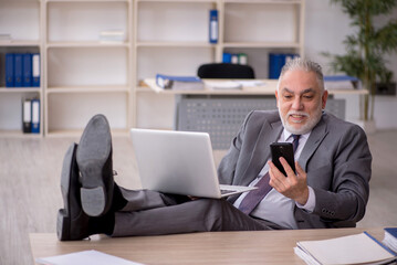 Old male employee speaking by phone at workplace