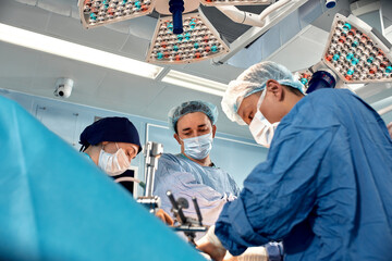 Low angle view of surgeons leaned over patient during complex surgical operation in a sterile operating room. Doctors are focused and extremely attentive. Modern medicine, saving patient's life.