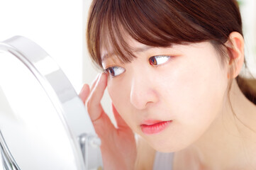 鏡を見ながら顔のスキンケアをする若い女性