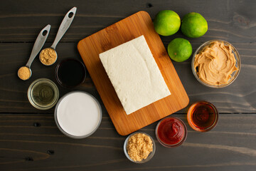 Tofu Satay with Peanut Sauce Ingredients on a Wood Table: Bean curd surrounded with limes, peanut...
