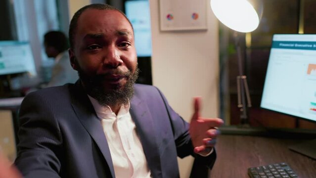 African american businessman using smartphone on selfie mode to make vlog of daily company internal tasks in office. POV shot of employee at work filming himself explaining business related info