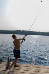 Childhood Delights: A Young Boy Enjoying Serene Fishing Moments from the Wooden Deck, Gently Casting His Fishing Rod into the Tranquil Waters of the Glittering Lake