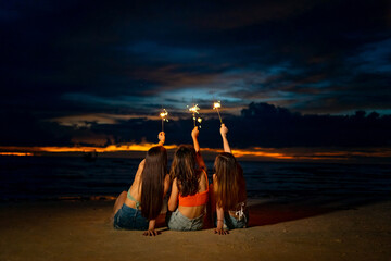Group of Young Asian woman friends playing sparklers firework together at tropical island beach in...