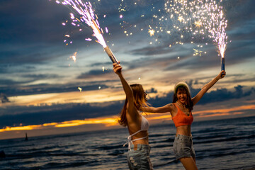 Group of Young Asian woman friends playing sparklers firework together at tropical island beach in...