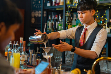 Professional Asian man bartender preparing and serving cocktail drink to customer on bar counter at...