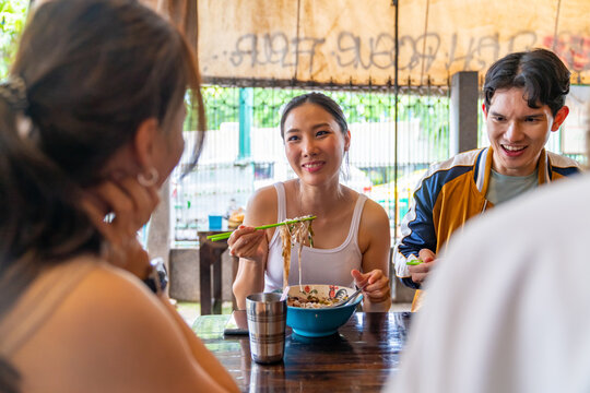 Young Asian Couple Enjoy And Fun Outdoor Lifestyle Shopping At Street Market On Summer Vacation. Man And Woman Couple Eating Street Food Noodle For Lunch Together While Shopping At Weekend Market.