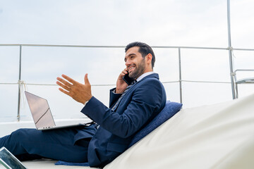 Confident businessman working on laptop computer and talking on mobile phone for global corporate...