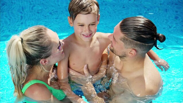 Mother with father and son resting and swimming in a pool in summer, happy family kissing