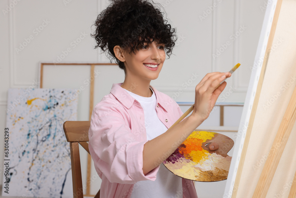 Poster Young woman painting on easel with canvas in studio