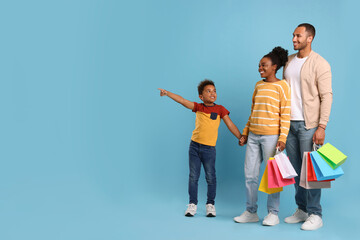 Family shopping. Happy parents and son with colorful bags on light blue background, space for text