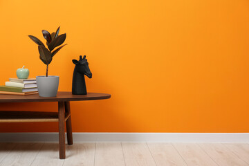 Wooden coffee table with different decor near orange wall indoors, space for text. Stylish interior design - Powered by Adobe