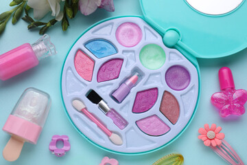 Decorative cosmetics for kids. Eye shadow palette, lipsticks, accessories and flowers on light blue...