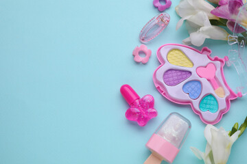 Decorative cosmetics for kids. Eye shadow palette, lipsticks, accessories and flowers on light blue...