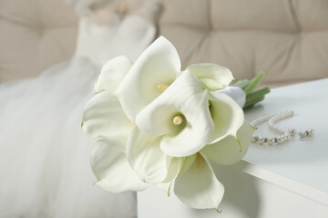 Obraz na płótnie Canvas Beautiful calla lily flowers tied with ribbon and jewelry on white chest of drawers indoors