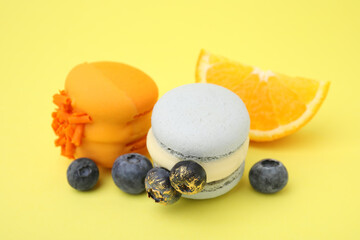 Delicious macarons, blueberries and orange slice on yellow background, closeup