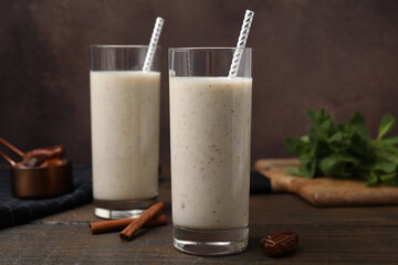 Glasses of delicious date smoothie, dried fruit and cinnamon on wooden table