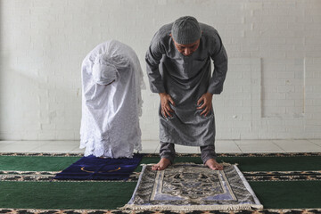 Front view of muslim couple wearing  praying salah together in mosque doing ruku movement, kneeling