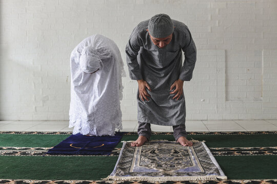 Front view of muslim couple wearing  praying salah together in mosque doing ruku movement, kneeling