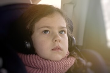 pensive young girl watching cartoons in headphones while traveling in a car