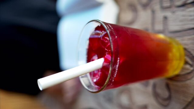 Red bubble tea with boba in a glass with ice and big white straw close up slow motion, vertical screen